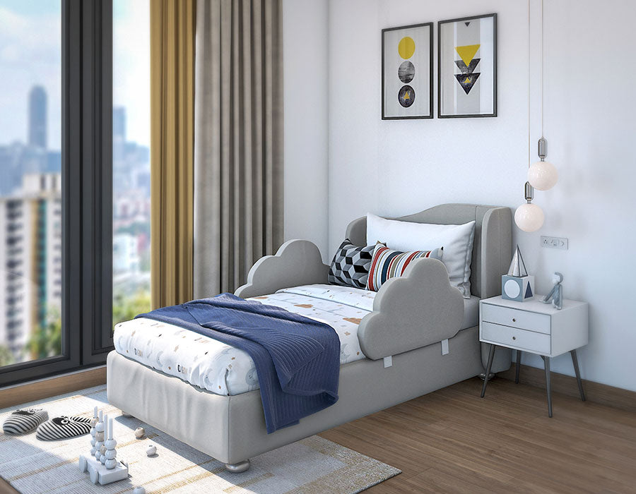 Modern child's bedroom featuring a grey bed with cloud-shaped side rails, colorful car-themed bedding, and an array of cozy pillows. The room is bright with a large window offering a city view, complemented by light curtains and hardwood flooring. A white bedside table with books and a blue alarm clock sits under contemporary pendant lights, adding charm to this playful and inviting space.