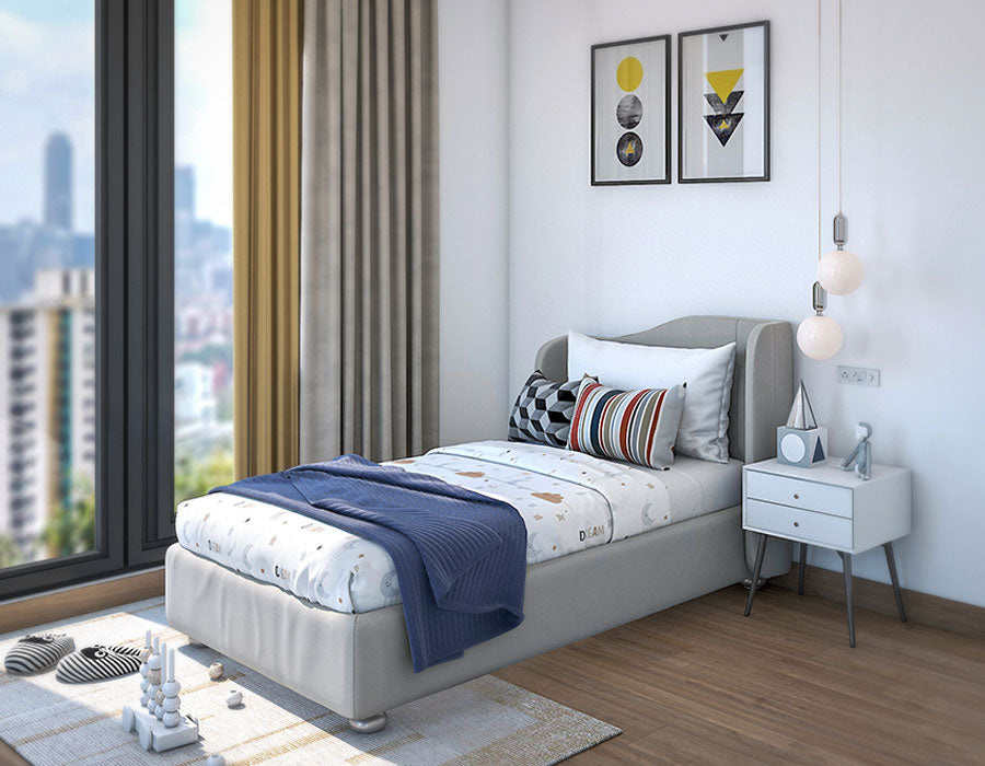 Modern child's bedroom featuring a grey bed, colorful car-themed bedding, and an array of cozy pillows. The room is bright with a large window offering a city view, complemented by light curtains and hardwood flooring. A white bedside table with books and a blue alarm clock sits under contemporary pendant lights, adding charm to this playful and inviting space.
