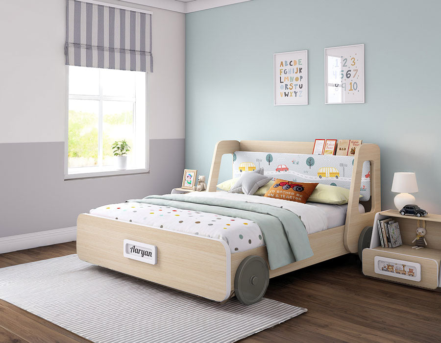 Stylish kids' bed with a playful car theme, featuring light wood accents and fabric upholstery with colorful car prints. The bed is personalized with the name 'Aaryan' on the footboard. Set in a modern children's room with pastel walls, framed educational posters, and a cozy side table, the bed blends functionality with fun. Ideal for kids, the design includes a book rack on the headboard for easy access to bedtime stories.