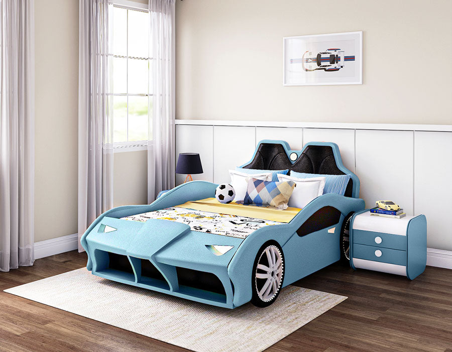 Blue car-themed children's bed in a modern bedroom with wooden flooring and light-colored walls. The bed features a sporty design with sleek curves, large wheel details, and a cushioned headboard resembling car seats. The bed is styled with colorful pillows and a playful bedding set, alongside a matching blue nightstand with drawers. A framed car illustration hangs on the wall, complementing the automotive theme.