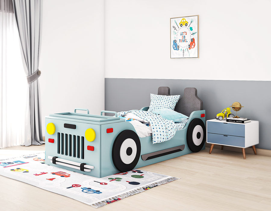 Bright and playful children's bedroom featuring a jeep-themed bed in light blue with realistic details such as headlights, wheels, and a front grille. The bed includes a lift-up mechanism for storage. The room is decorated with a fun rug, a white and blue bedside table with a yellow toy truck, and a wall art that reads 'Let's Go Travel.' Natural light pours in through large windows with light curtains, creating a cheerful and adventurous space for a child.