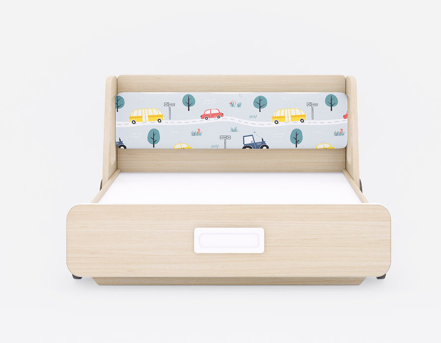 Front view of a kids' bed with light wood finish, featuring a playful car-themed fabric headboard. The headboard showcases colorful vehicles and road signs, creating a fun and engaging design for children. The footboard includes a recessed handle for easy access, combining style with functionality. Perfect for a modern children's room, this bed offers both comfort and charm.