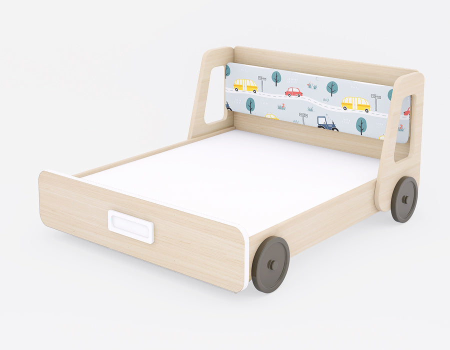 Angled view of a children's bed with a light wood finish, featuring a playful vehicle-themed headboard. The headboard showcases colorful cars, buses, and road signs, creating a vibrant and engaging design. The bed frame includes cutout side panels and rounded wheels, adding a fun, automotive-inspired touch. A recessed handle on the footboard enhances accessibility, blending functionality with a modern look, perfect for kids' rooms.