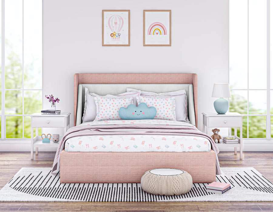 Bright and cozy children's bedroom featuring a pink-colored upholstered bed with a high headboard. The bed is adorned with playful pillows, including a polka dot pattern and a toy. The room has large windows letting in natural light, two white bedside tables with decorative items, and wooden flooring. Wall art with positive messages adds a cheerful touch to the inviting space.